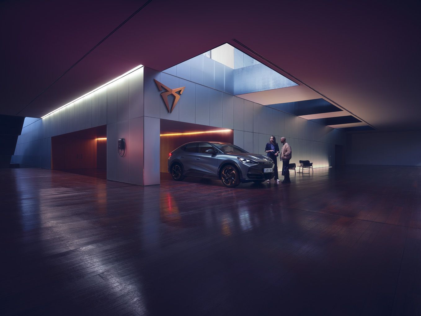 A three quarter view of the new CUPRA Tavascan VZ blue parked in a CUPRA showroom with a customer and CUPRA Master standing close to the car.