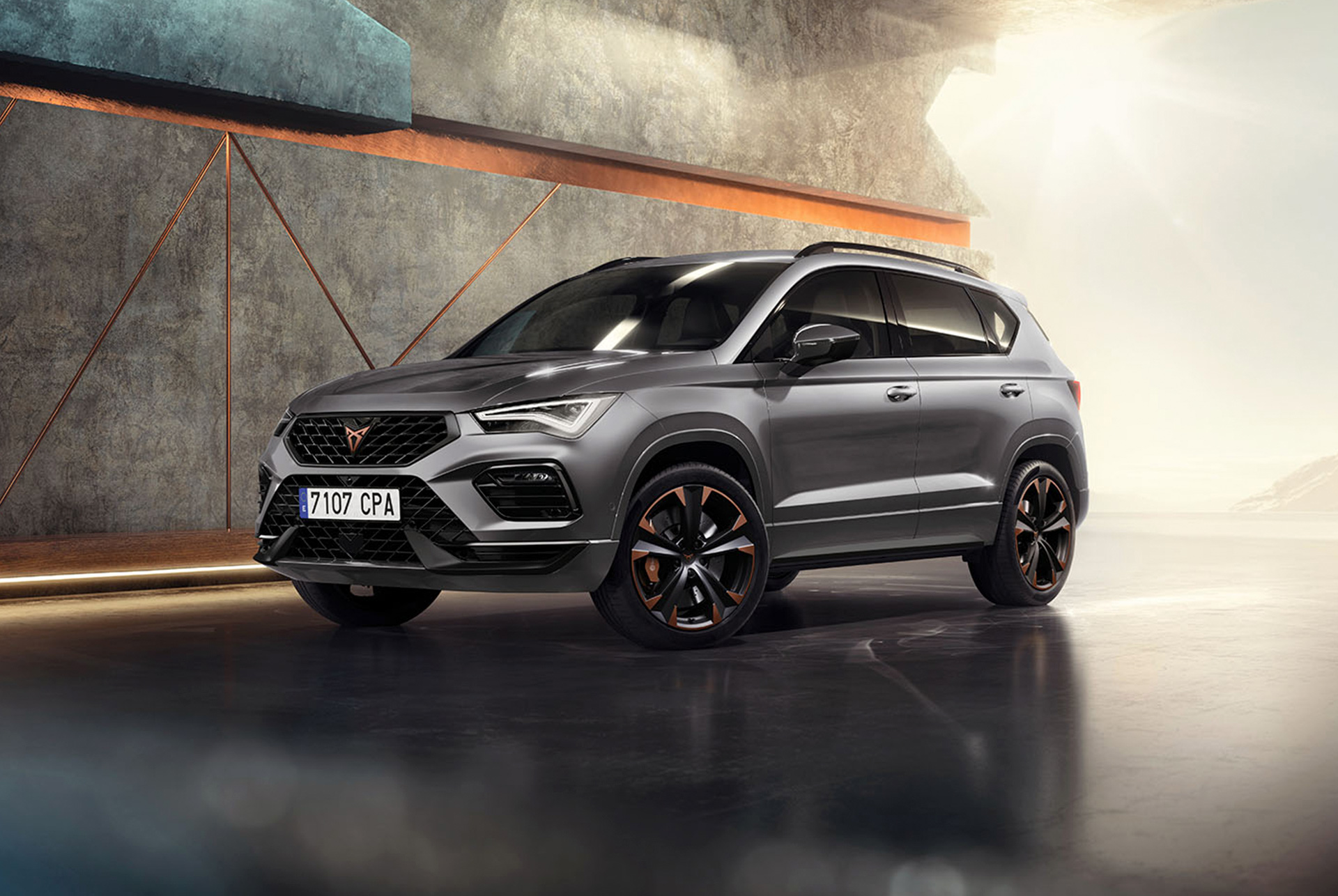 cupra ateca in graphite grey, a sporty and suv parked in a modern, industrial setting. The car design features aerodynamic lines, led headlights and distinctive alloy wheels with copper accents. The background includes a geometric wall design, contrasting with the sleek vehicle design.