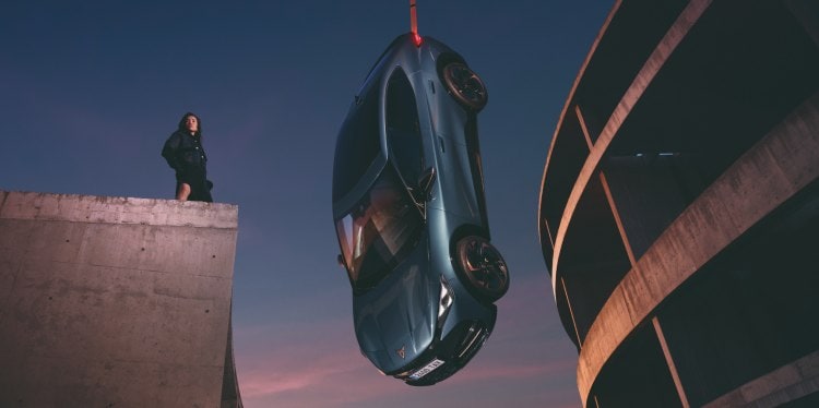 Cupra tavascan hanging at concrete setting with sky backdrop and model.