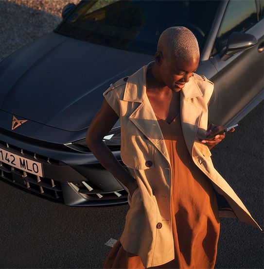 A cupra leon hatchback in magnetic tech matt grey with driver analysing driving data via her mobile phone.