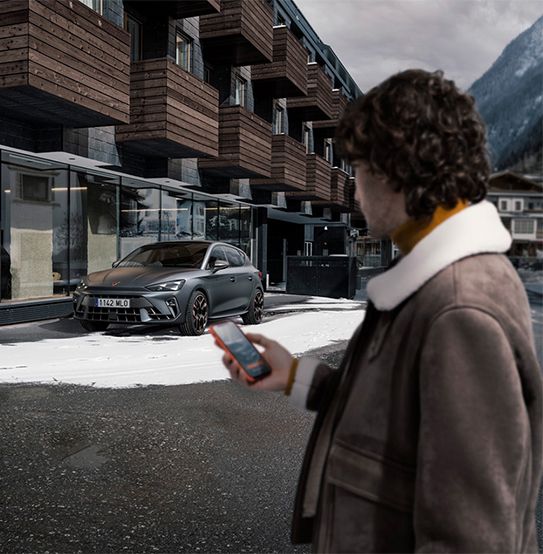 Cupra leon hybrid hatchback parked in a snowy urban setting, with a person holding a smartphone in the foreground, locating the car with the my cupra app.